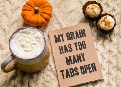 foto van een kop koffie, 2 koekjes, een pompoen en een boek met de tekst 'my brain has too many tabs open'