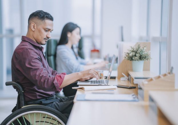 Persoon van kleur in rolstoel kijkt naar scherm laptop